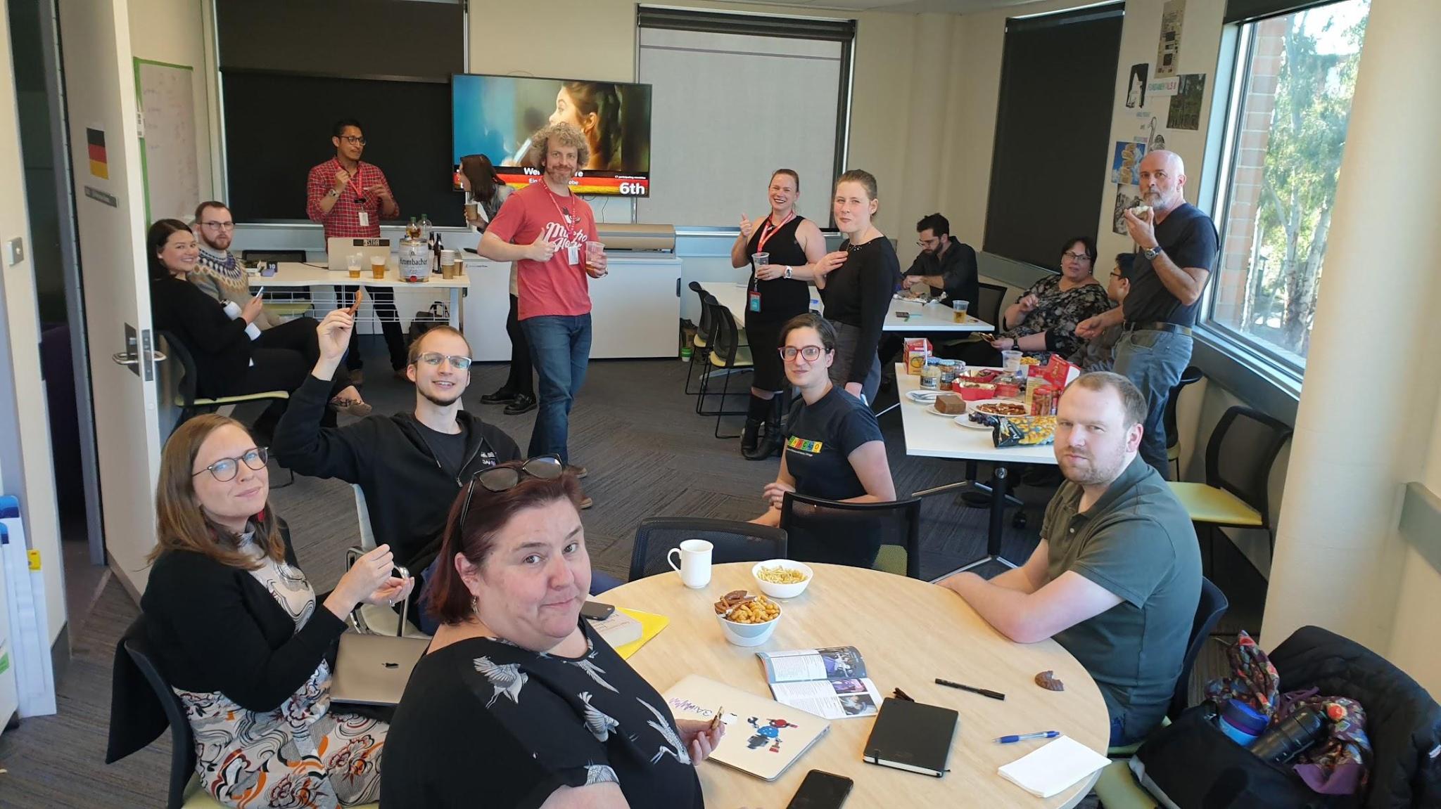 people in a classroom sitting in groups at tables and looking at the camera.