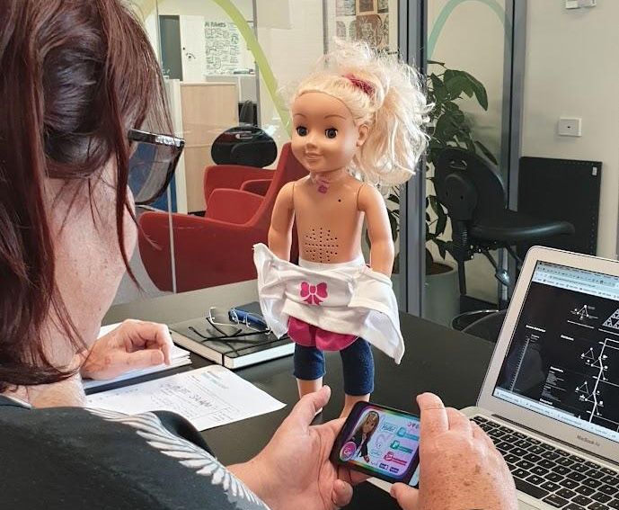 A doll similar to Barbie stands on a desk while Alison programs it