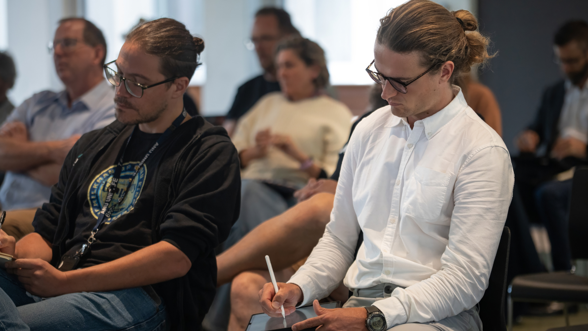 two men take notes in a crowd