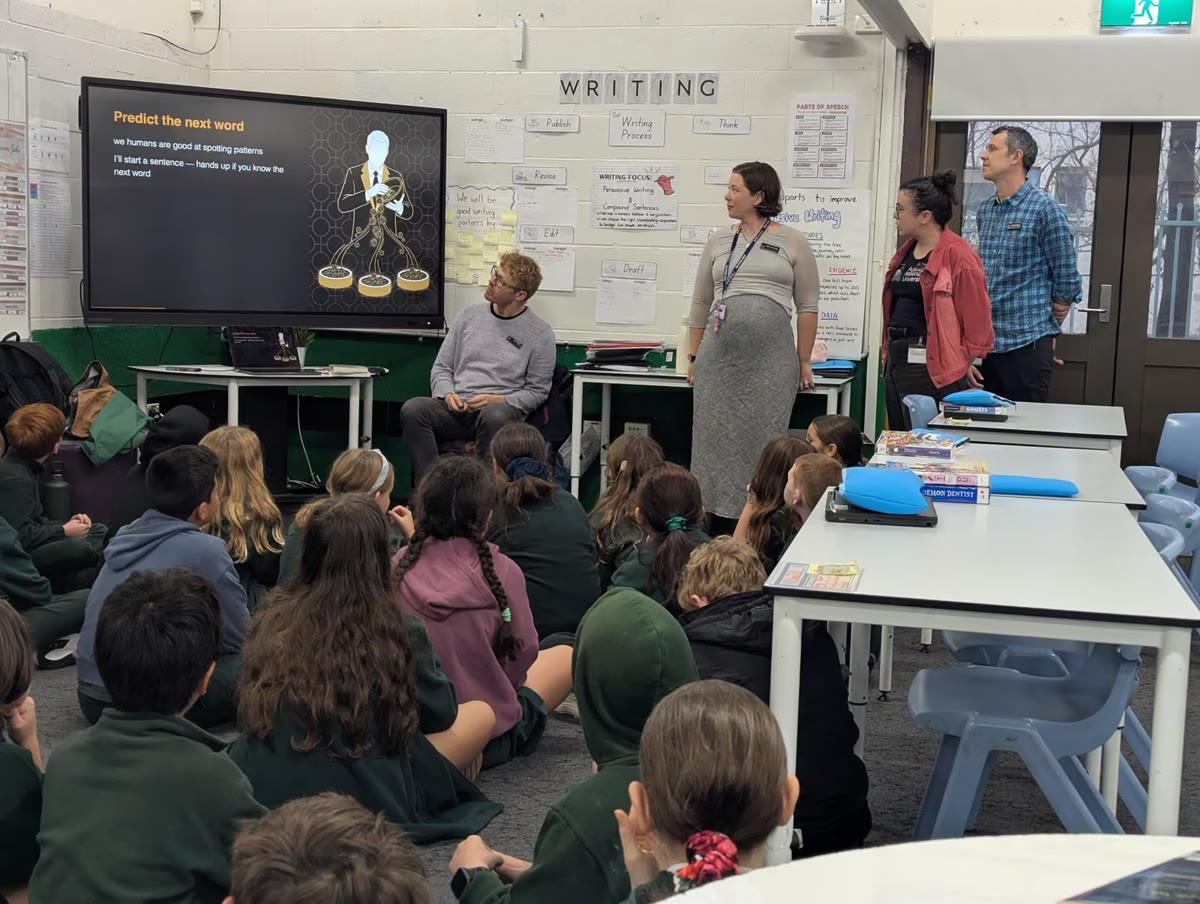 Duffy Primary Year 5 students seated facing the front of the room as two facilitators present a slide headed “Writing”
